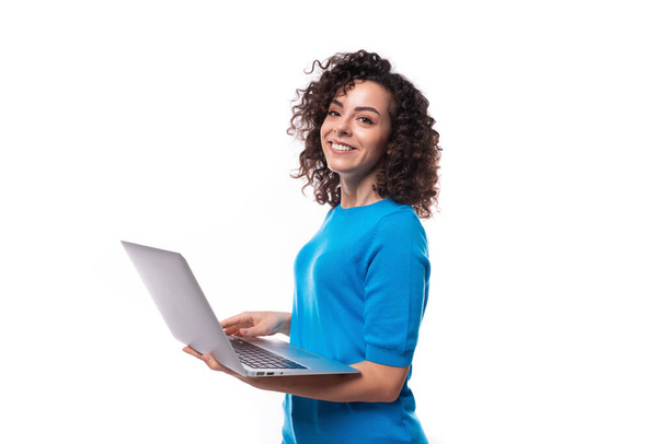 nuori nainen, jolla on kihara kampaus pukeutunut siniseen T-paitaan, työskentelee kannettavassa tietokoneessa. - Valokuva, kuva