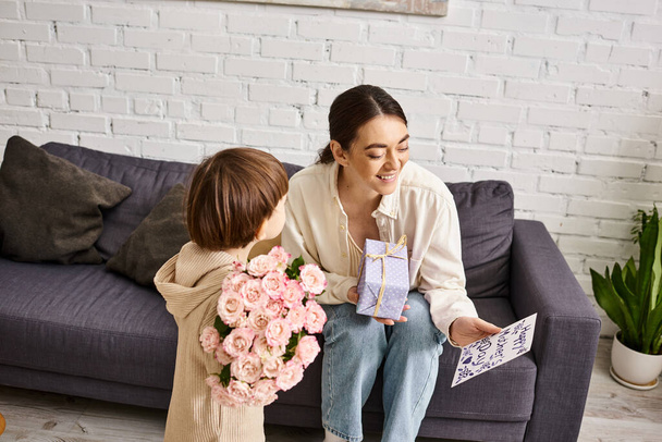 lindo niño pequeño dando su alegre mamá presente y postal con ramo de flores en el día de las madres - Foto, imagen