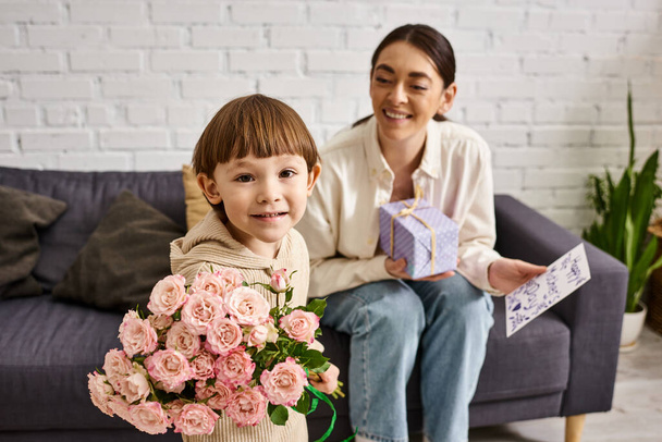 adorable niño pequeño dando a su mamá regalo y postal con ramo de flores en el día de la madre - Foto, imagen