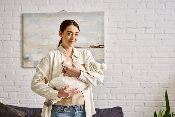 madre alegre de buen aspecto en ropa de casa sosteniendo amorosamente a su bebé recién nacido, crianza moderna - Foto, Imagen