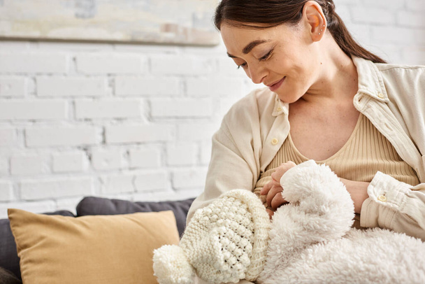 ansprechende fürsorgliche fröhliche Mutter in kuscheliger Hauskleidung, die ihr neugeborenes Kind stillt, moderne Elternschaft - Foto, Bild