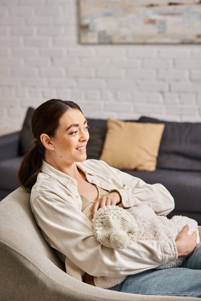 good looking cheerful woman in pastel homewear with jeans sitting and breastfeeding her baby boy - Fotoğraf, Görsel