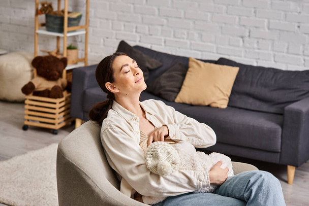 attraente donna allegra in casa pastello con jeans seduta e allattamento al seno il suo bambino - Foto, immagini