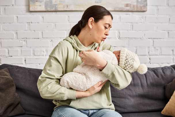 ソファーで彼女のかわいい新生児を慰めるホームウェアで良い見て愛情のある母親,現代の育児 - 写真・画像