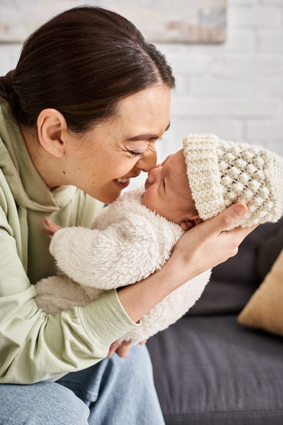 веселая привлекательная женщина в уютной домашней одежде с очаровательным новорожденным мальчиком, современным воспитанием - Фото, изображение