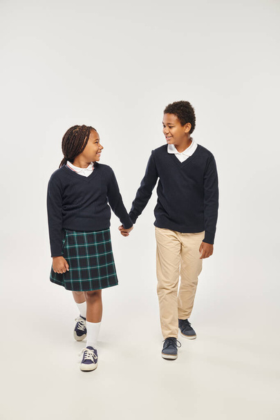 Üniformalı Afro-Amerikan okul çocukları gri arka planda el ele tutuşuyorlar. - Fotoğraf, Görsel