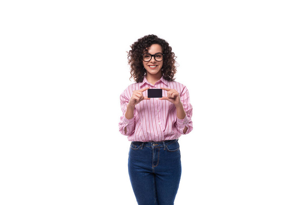 young beautiful curly brunette woman in pink shirt holding plastic card mockup. - Photo, Image