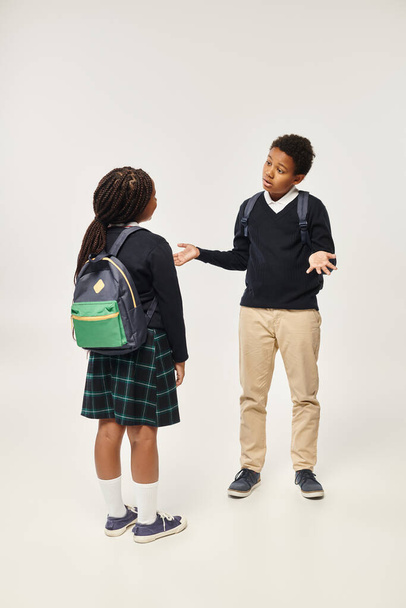 scolari afroamericani con zaini in piedi insieme e chattare su sfondo grigio - Foto, immagini