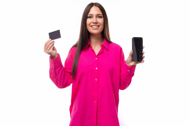 csinos fiatal barna fényes rózsaszín ing gazdaság hitelkártya mockup és okostelefon fehér háttér másolási hely. - Fotó, kép