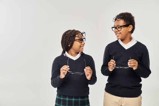 щасливі афроамериканські школярі в окулярах тримають окуляри на сірому фоні - Фото, зображення