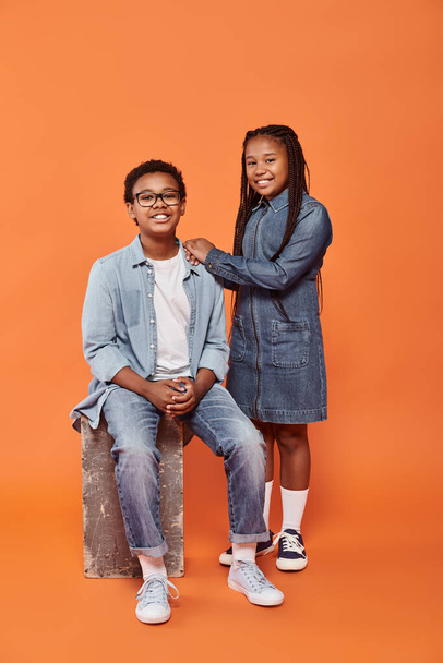 felice bambini africani americani in abbigliamento casual denim posa insieme su sfondo arancione - Foto, immagini