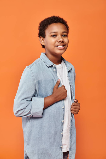 vidám afro-amerikai fiú alkalmi ruhában pózol boldogan és mosolyog a kamera előtt narancssárga háttérrel - Fotó, kép