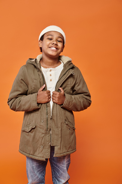 カメラで幸せに笑顔のビーニー帽子と冬服で陽気なアフリカ系アメリカ人の少年 - 写真・画像
