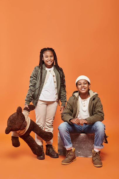 joyous preteen african american girl with braids and boy with beanie hat smiling at camera - Photo, Image