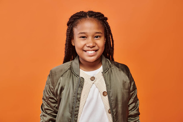 vidám afro-amerikai lány téli öltözékben vidáman mosolyog a kamerába narancssárga háttérrel - Fotó, kép