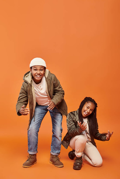 cheerful african maerican children in warm winter jackets posing in motion on orange backdrop - Photo, Image