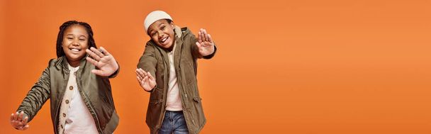 niños afroamericanos alegres en trajes calientes posando en movimiento y sonriendo a la cámara, pancarta - Foto, imagen