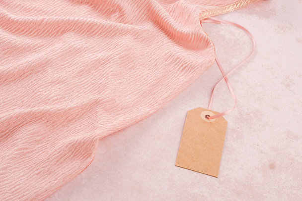 Табличка с одеждой, макет. Красивый персиковый цвет текстуры одежды. Ответственное потребление. Экологичность и устойчивая мода. Высокое качество фото - Фото, изображение