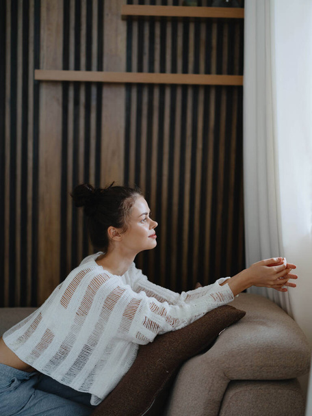 Mujer en suéter y pantalones de casa relajante tumbado en el sofá en casa, acogedor día libre con comodidad, estilo de vida real con una sonrisa. Foto de alta calidad - Foto, Imagen