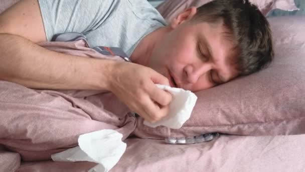Καυκάσιος στο κρεβάτι με ιό, γρίπη ή κρύα μύτη περιτριγυρισμένη από χρησιμοποιημένους ιστούς. Άρρωστος άντρας στο σπίτι - Πλάνα, βίντεο