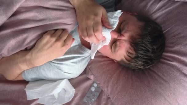 Ill caucasian young man sick with flu, cold or virus blowing running nose, got fever caught cold, sneezing in tissue lying in bed at home. Top view - Footage, Video