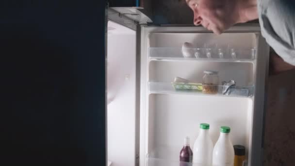 Caucasian hungry man at night open fridge searching food. Happy male on diet with night hunger taking and eating apple from refrigerator. Insomnia concept - Footage, Video
