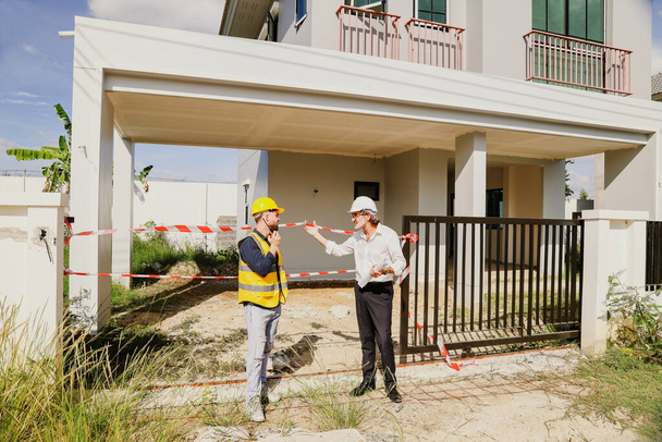 Senior architect talks with workers and safety officers housing construction project taped prevent entry due to dangers during construction warning careful prevent danger in order to reduce accidents. - Foto, afbeelding