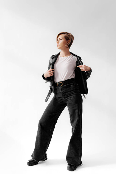 Donna sicura di sé in mostra una giacca di pelle e jeans svasati, un perfetto mix di moda retrò e contemporanea - Foto, immagini