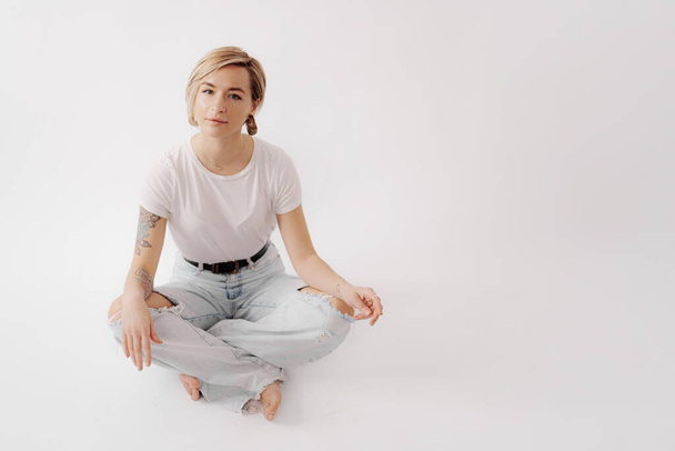 A serene young woman in a casual pose, wearing a white t-shirt and distressed jeans, exudes peaceful elegance - Photo, Image