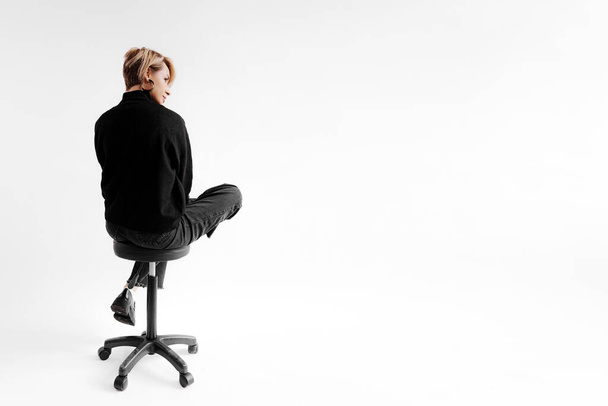 Una mujer en una pose relajada en una silla de oficina, su moda refleja un estado de ánimo reflexivo y sereno contra un fondo brillante - Foto, Imagen