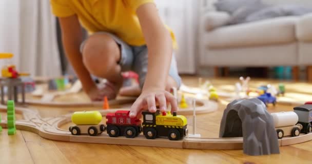 Egy fiú játszik a gyerekvasúttal. A gyerek fából készült játékokkal játszik a padlón. Egy játékvonat egy fából készült vasúton utazik. Kiváló minőségű 4k felvételek - Felvétel, videó