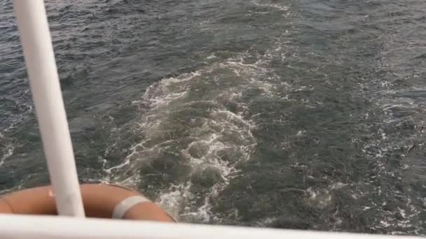 Blick von Deck und Seite durch Rettungsring des Bootes, das auf dem Meer segelt. Schiff schneidet durch schäumend weiße Wellen des tiefblauen Meeres. Weiße Blase durch beweglichen Propellermotor mit weißem Schaum ausgeworfen - Filmmaterial, Video
