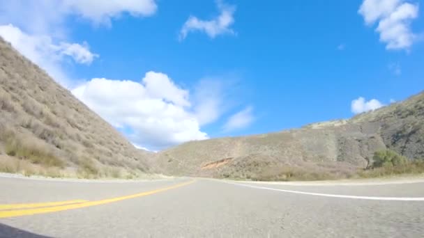 Pojazd porusza się wzdłuż autostrady Cuyama w jasnym słońcu. Otaczający krajobraz oświetlony jest promieniującym słońcem, tworząc malowniczą i zachęcającą scenę podczas podróży samochodem. - Materiał filmowy, wideo