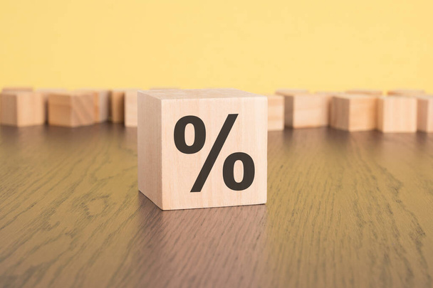 a wooden cube with a percentage sign rests on the brown table, against a yellow background. copy space - Photo, Image