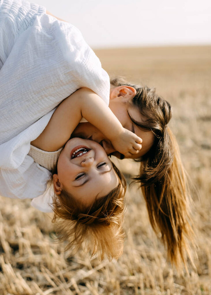 Moeder spelen met haar dochtertje buiten in een veld, houden haar in de armen, kussen op de wang. - Foto, afbeelding