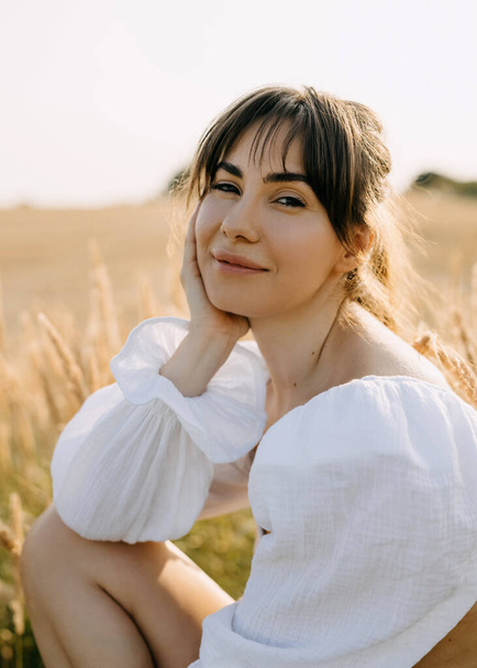 jonge vrouw zitten in een veld met hoog droog gras, kijken naar de camera, glimlachen. - Foto, afbeelding
