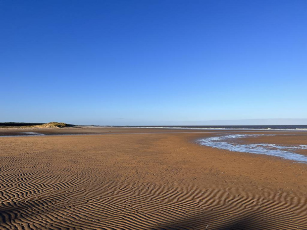 Prachtig landschap van het strand bij Holkham met zwembad van zeezout water tussen grazige zandbanken op koude rustige heldere Winterdag met blauwe luchten in Norfolk East Anglia uk op vakantie wandeling - Foto, afbeelding