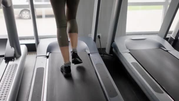 Egy lány atléta lépéseket tesz egy futópadon. Egy nő felmelegíti a lábizmait edzés előtt. Könnyű fizikai aktivitás sportfelszereléssel. Közelről. Kiváló minőségű 4k felvételek - Felvétel, videó