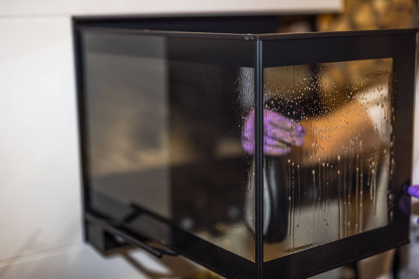 Vista da mão de uma mulher limpando fuligem do vidro da lareira. - Foto, Imagem