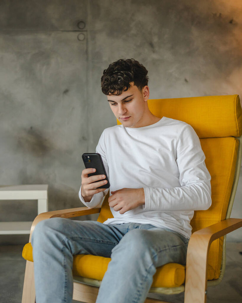 ένα έφηβος αγόρι χρησιμοποιούν το κινητό τηλέφωνο για να παίξετε online βιντεοπαιχνίδια στο σπίτι - Φωτογραφία, εικόνα