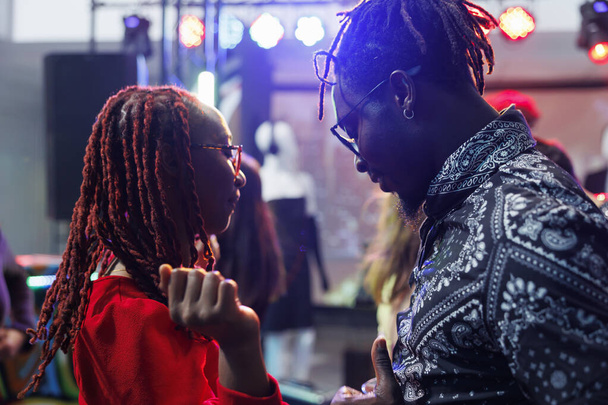 Young couple dancing together while partying and relaxing in nightclub. African american man and woman moving to music sound on dancefloor while attending social gathering in club - Photo, Image