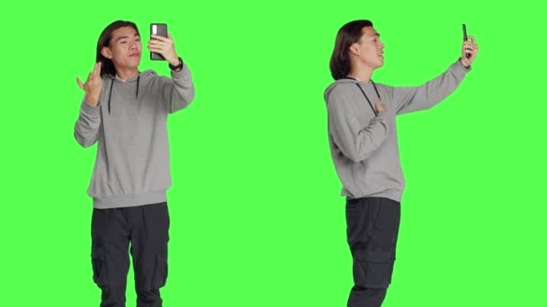 Arkadaşlarıyla video bağlantısı olan Asyalı bir adam yeşil ekrana karşı telefon kamerasıyla insanları aramak için akıllı telefon kullanıyor. Erkek model video konferans ağında biriyle konuşuyor. - Video, Çekim