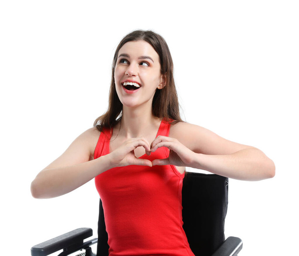 Young woman in wheelchair making heart gesture on white background - Photo, Image
