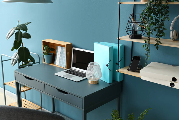 Стильне робоче місце з сучасним ноутбуком, канцелярським приладдям та лампою біля кольорової стіни - Фото, зображення