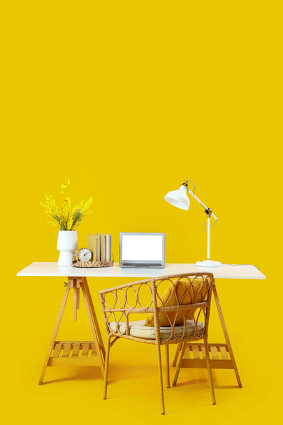 Modern dizüstü bilgisayarı ve sarı arka planda mimoza çiçekleri olan şık bir iş yeri. - Fotoğraf, Görsel