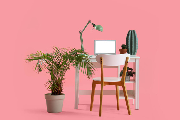 Stylové pracoviště s moderním notebookem a krásnými pokojovými rostlinami na růžovém pozadí - Fotografie, Obrázek