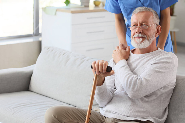 Uomo anziano con bastone da passeggio e infermiera a casa - Foto, immagini