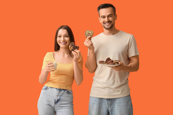 Молода пара зі смачним печивом і склянкою молока на помаранчевому фоні - Фото, зображення
