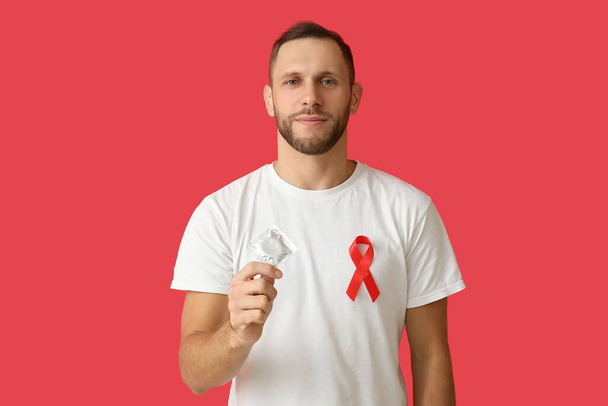 Young man with red ribbon and condom on color background. AID awareness concept - Photo, Image