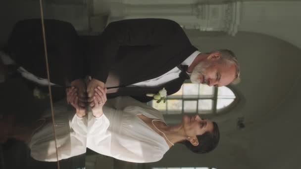 Pionowy średni portret szczęśliwej białej pary w średnim wieku, która właśnie wyszła za mąż, patrząc w kamerę, stojąc w kaplicy po ceremonii ślubnej. - Materiał filmowy, wideo